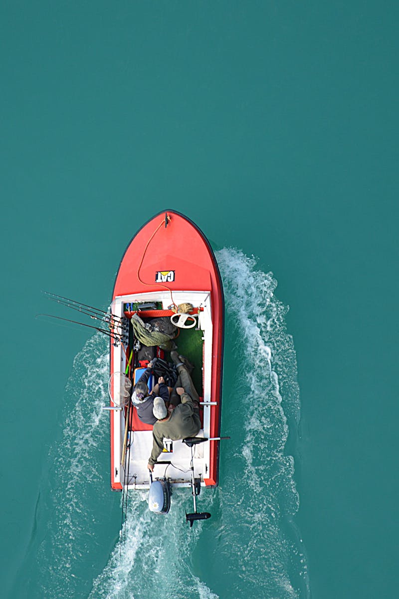 Top view of a red motorboat with fishermen navigating open turquoise waters.